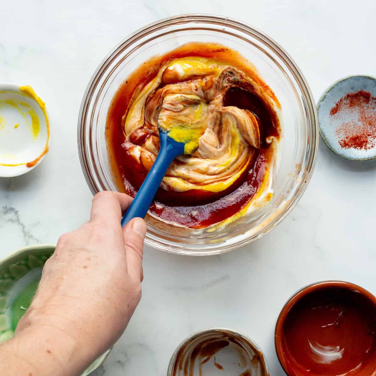 Stirring together the ingredients for burger special sauce in a glass bowl with a blue spatula.