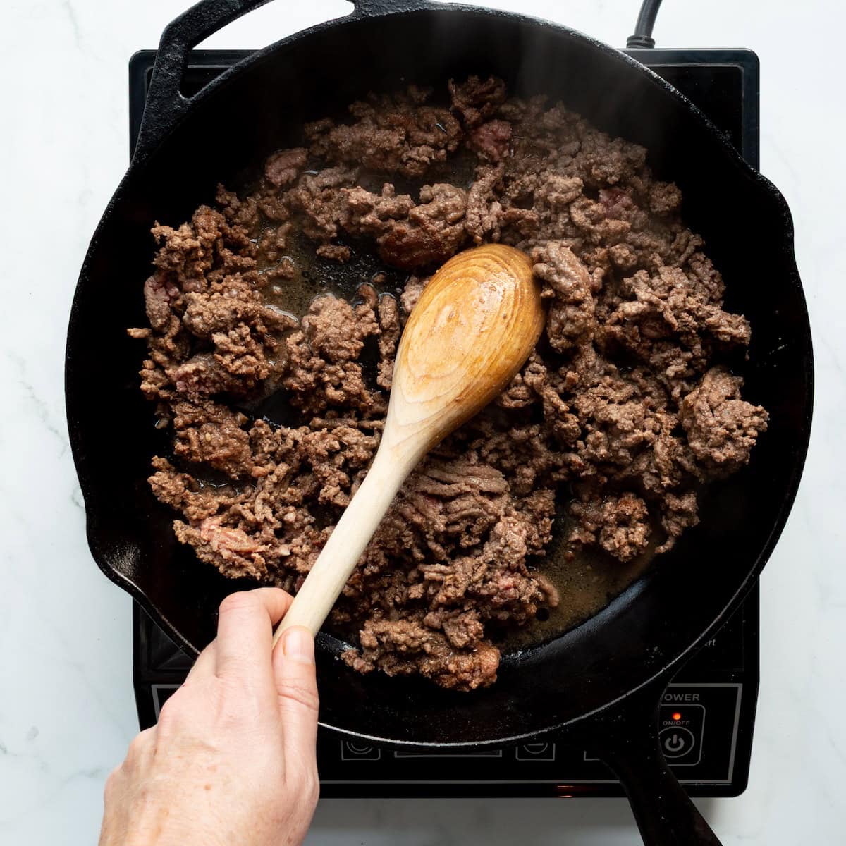 Browning ground beef in a cast-iron skillet.