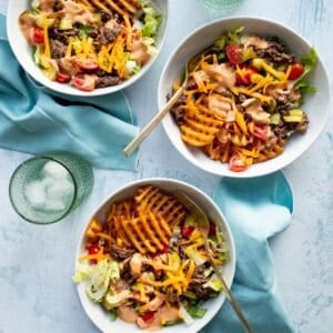 Three white bowls of Cheeseburger Bowls with Special Sauce with light blue napkins and green glasses of water.