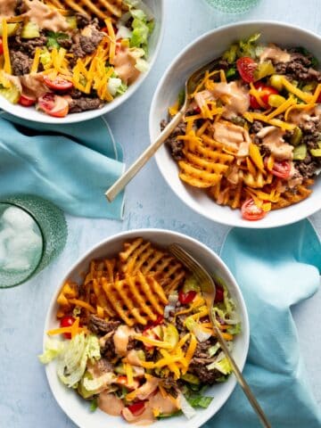 Three white bowls of Cheeseburger Bowls with Special Sauce with light blue napkins and green glasses of water.