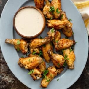 An oven metal tray topped with air fryer buffalo wild wings copycat lemon pepper chicken wings and a wooden bowl of white bbq sauce on the side.
