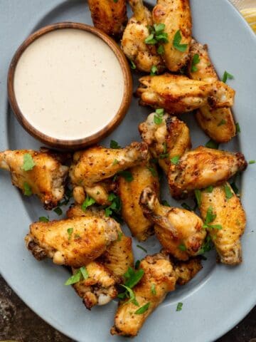 An oven metal tray topped with air fryer buffalo wild wings copycat lemon pepper chicken wings and a wooden bowl of white bbq sauce on the side.