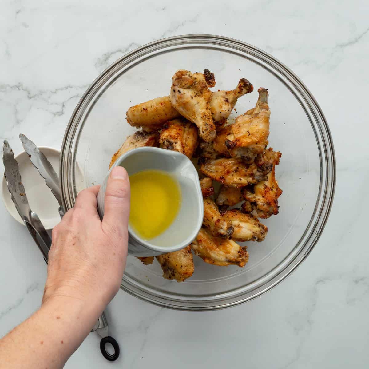 Pouring butter over air fryer lemon pepper chicken wings in a glass bowl.