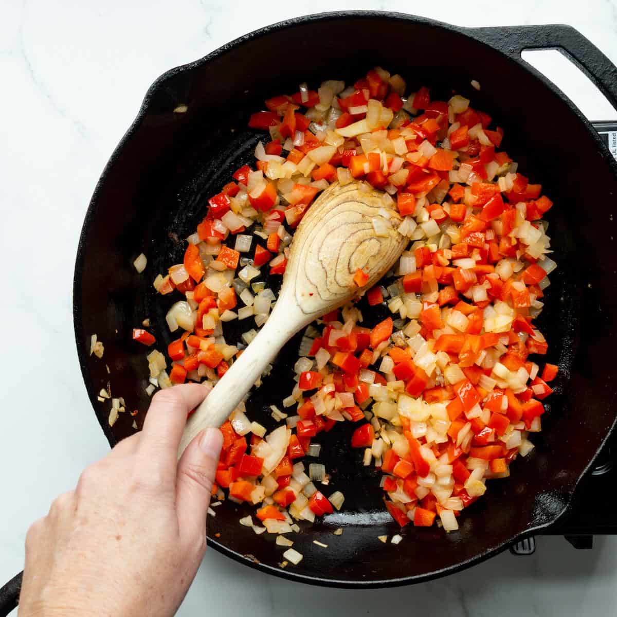Sautéing diced red bell pepper and onion in a cast iron skillet.