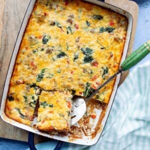 Sausage and Egg Casserole with Cottage Cheese in a navy blue handled casserole dish with a green handled spatula lifting out a square.