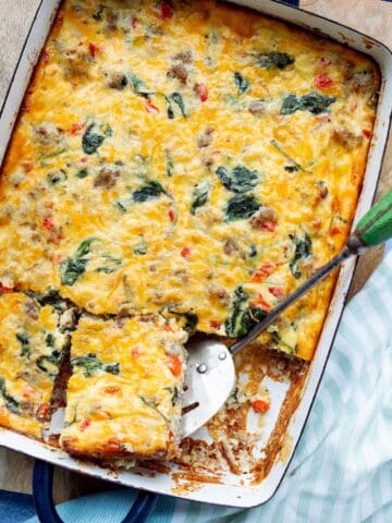 Sausage and Egg Casserole with Cottage Cheese in a navy blue handled casserole dish with a green handled spatula lifting out a square.