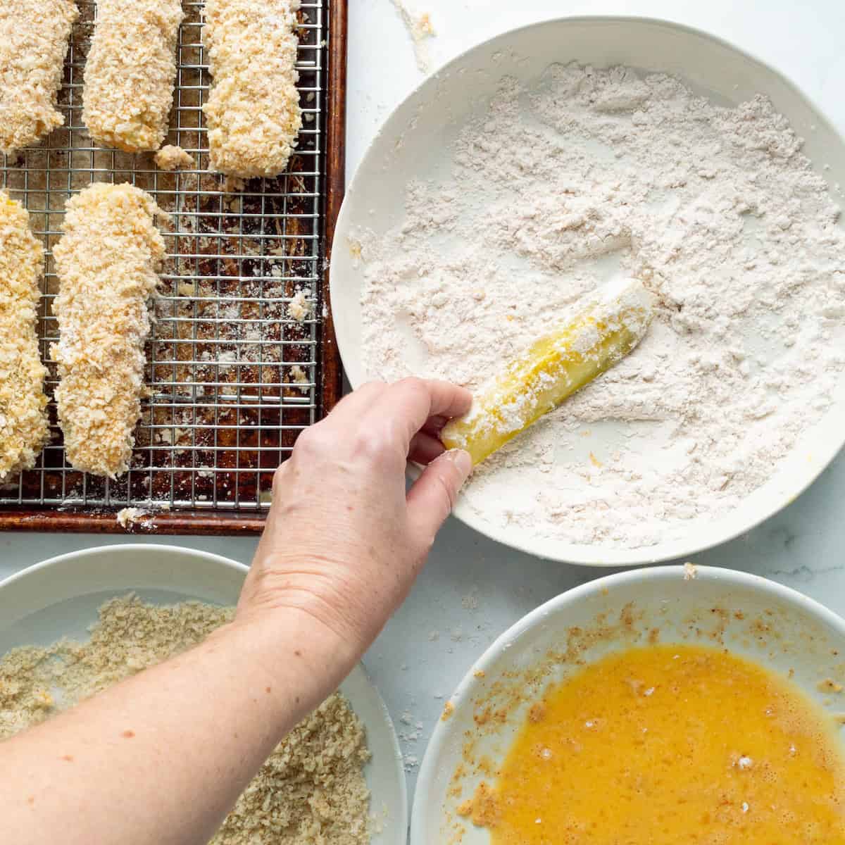 Dredging pickle spears in flour before dipping in egg wash and panko breadcrumbs for fried pickles.