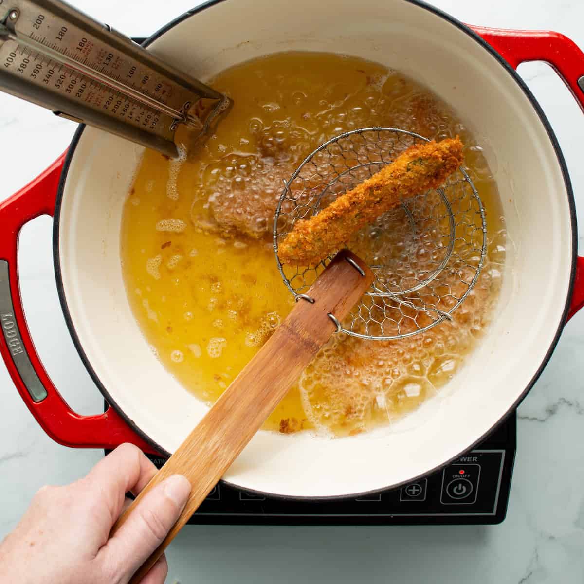 Deep frying fried pickle spears in a red handled Dutch oven.