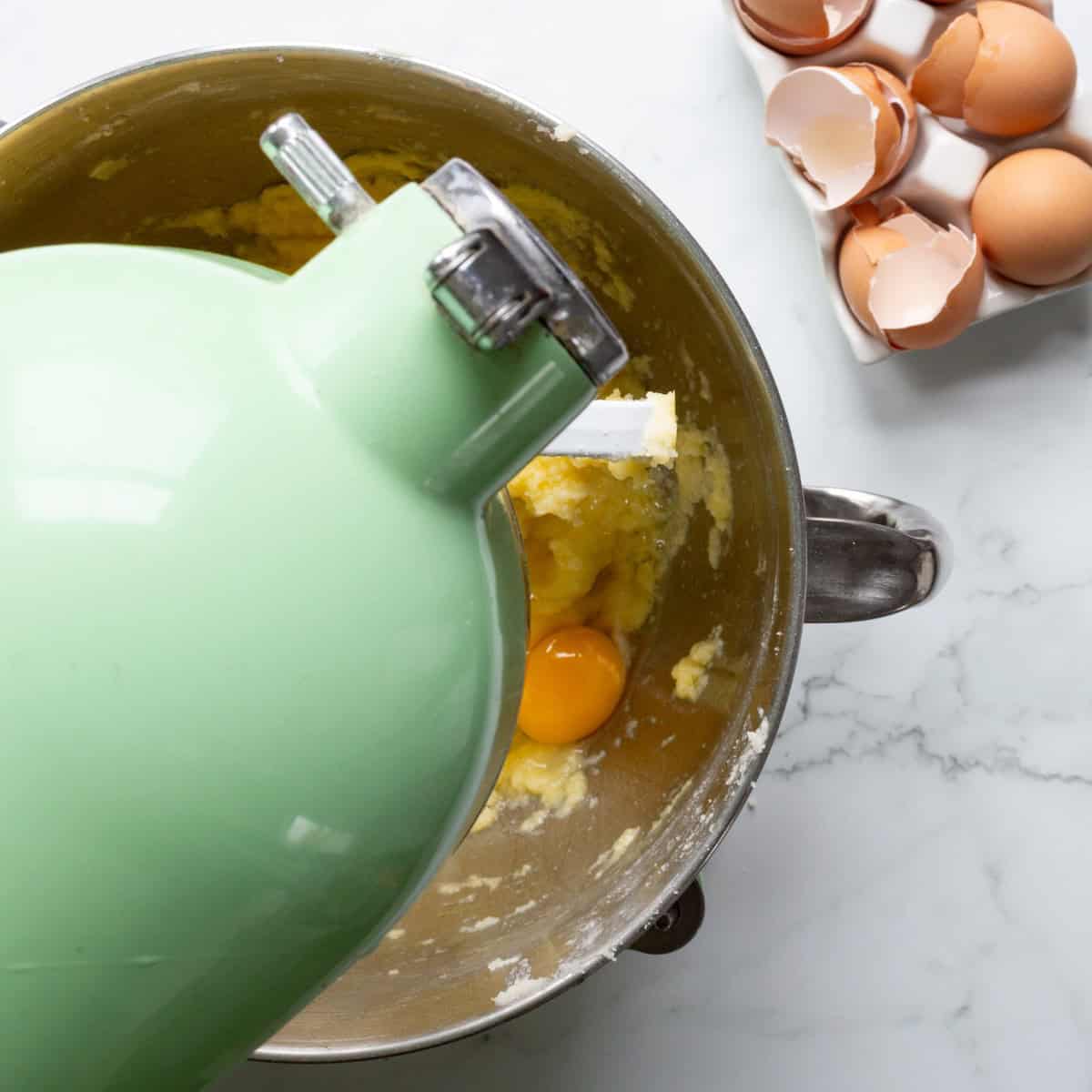 Adding eggs to pound cake batter in a green Kitchen mixer bowl.