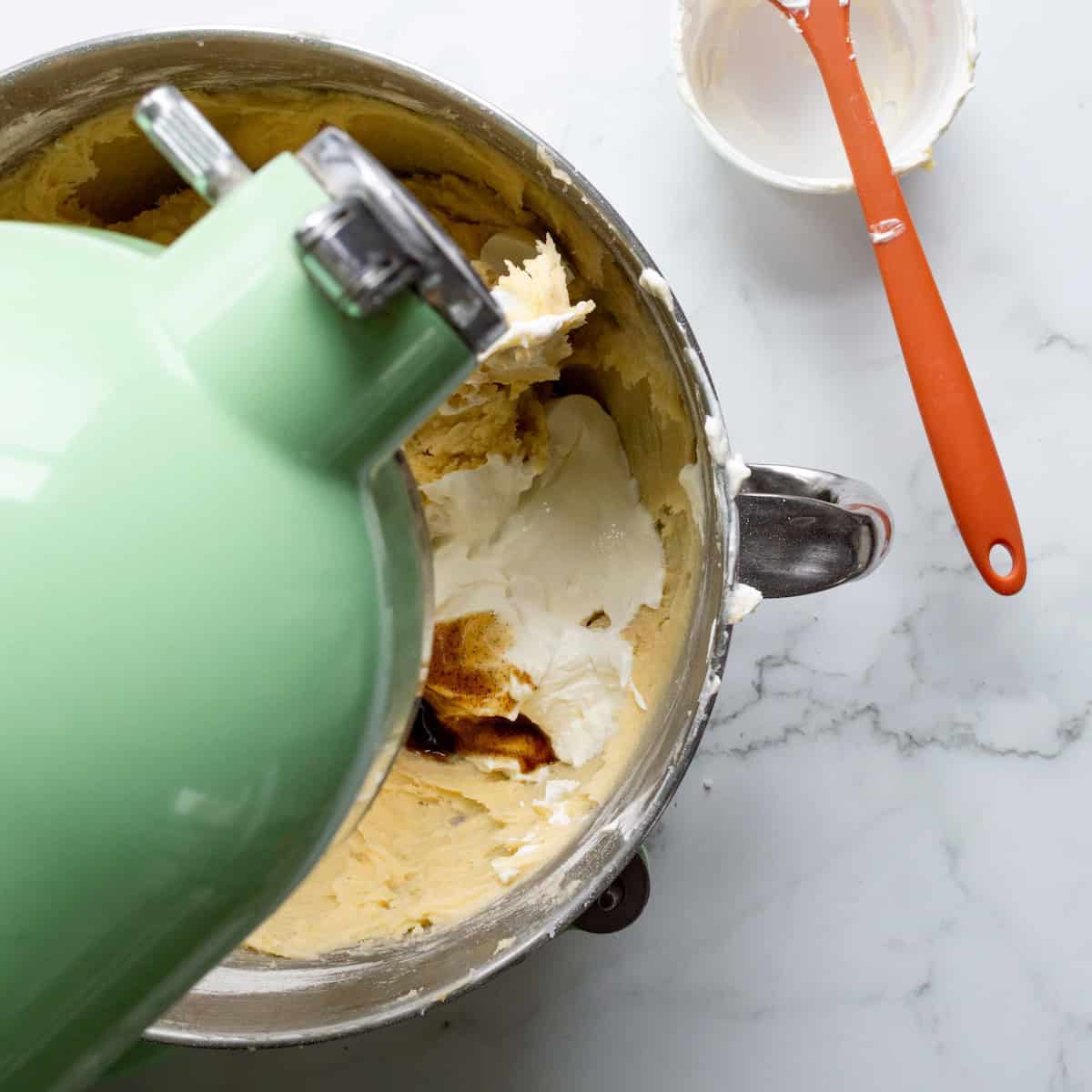 Adding sour cream and vanilla bean paste to sour cream pound cake batter in a light green mixer.