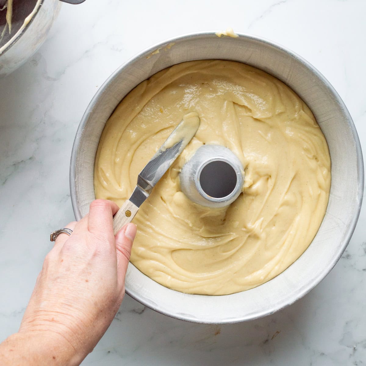 Spreading sour cream pound cake batter into a tube pan with an offset spatula.