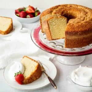 Southern sour cream pound cake on a cake stand with slices on plates topped with whipped cream and strawberries.