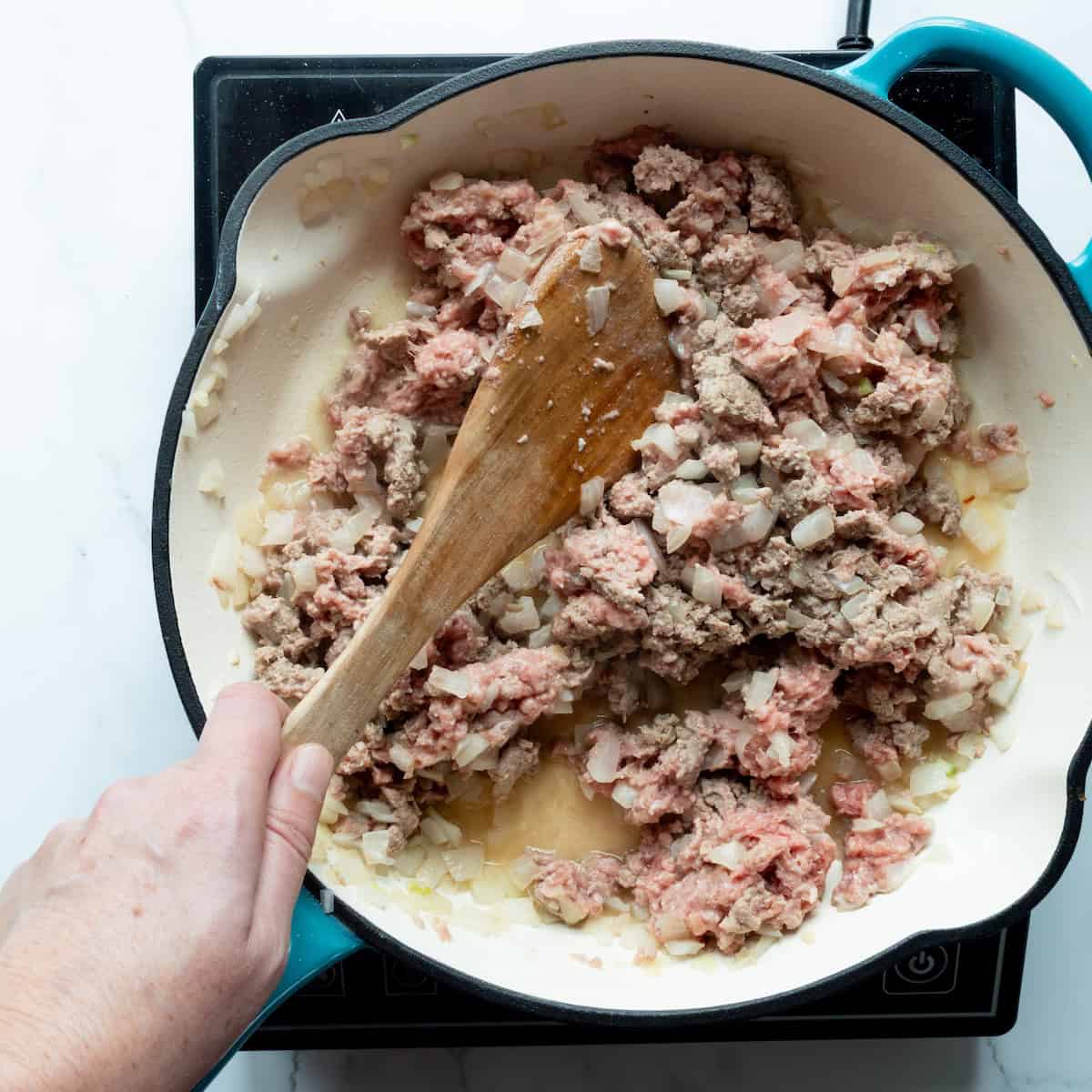 Browning turkey and onions in a blue-handled cast-iron skillet.