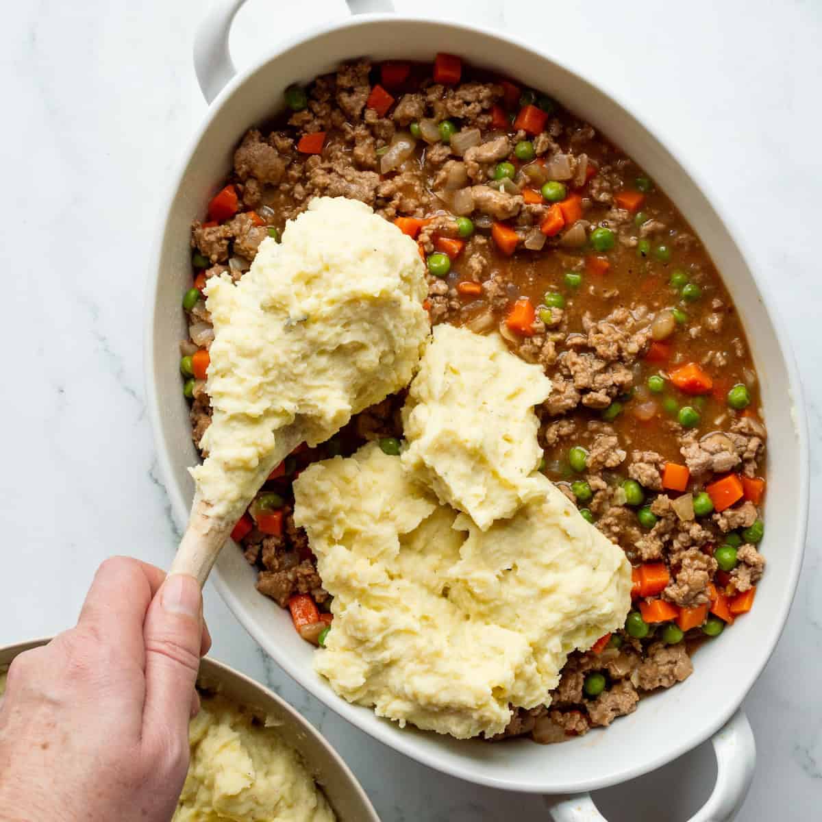 Scooping mashed potatoes onto the top of shepherd's pie filling.