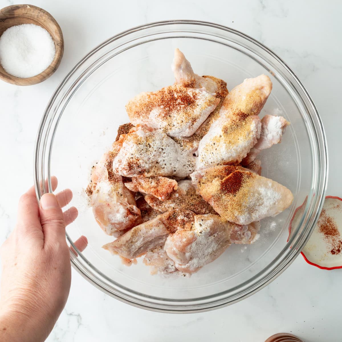 Seasoning chicken wings in a glass bowl.