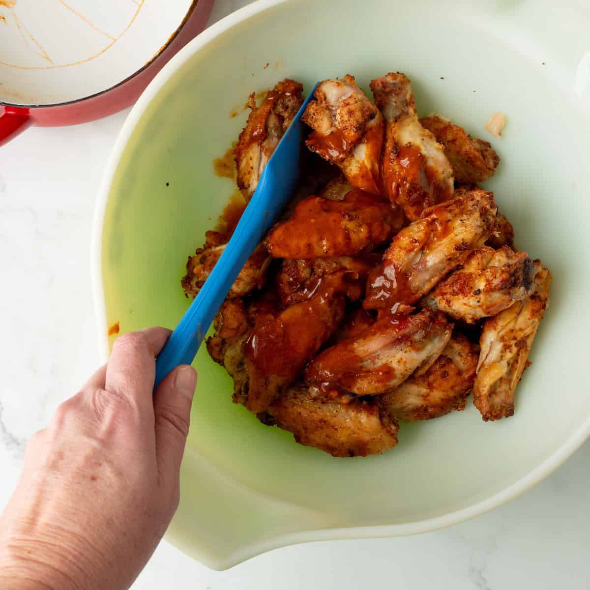Coating cooked crispy air fryer chicken wings with homemade buffalo wing sauce in a large bowl.