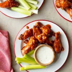 Foster Farms chicken wings (made in the air fryer) on red rimmed enamel plates with bowls of homemade ranch for dipping and celery sticks on the side.