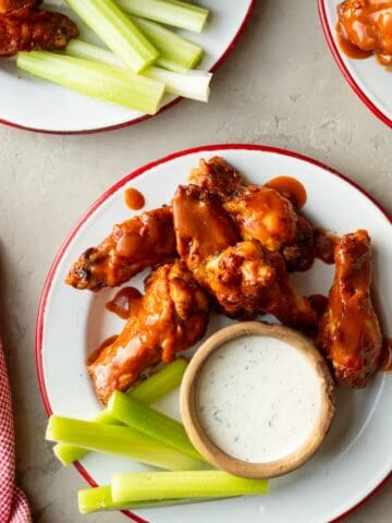 Foster Farms chicken wings (made in the air fryer) on red rimmed enamel plates with bowls of homemade ranch for dipping and celery sticks on the side.
