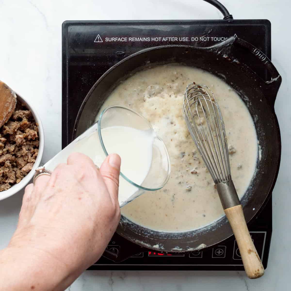 Pouring milk into a skillet of gravy.