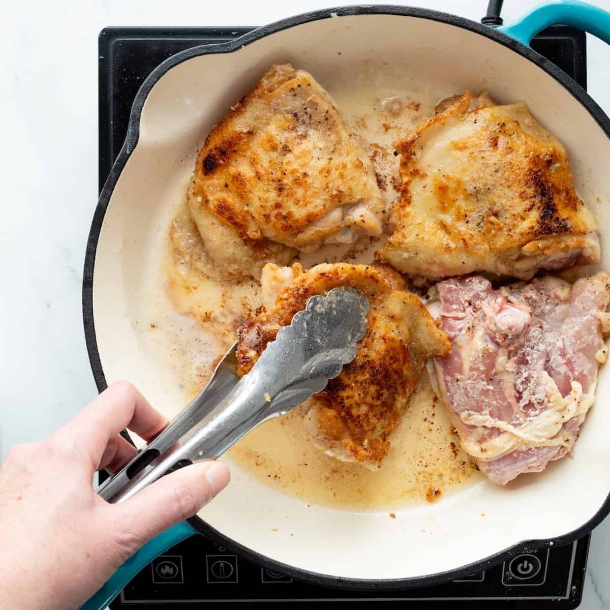 Browning chicken thighs in a blue enameled cast iron skillet.