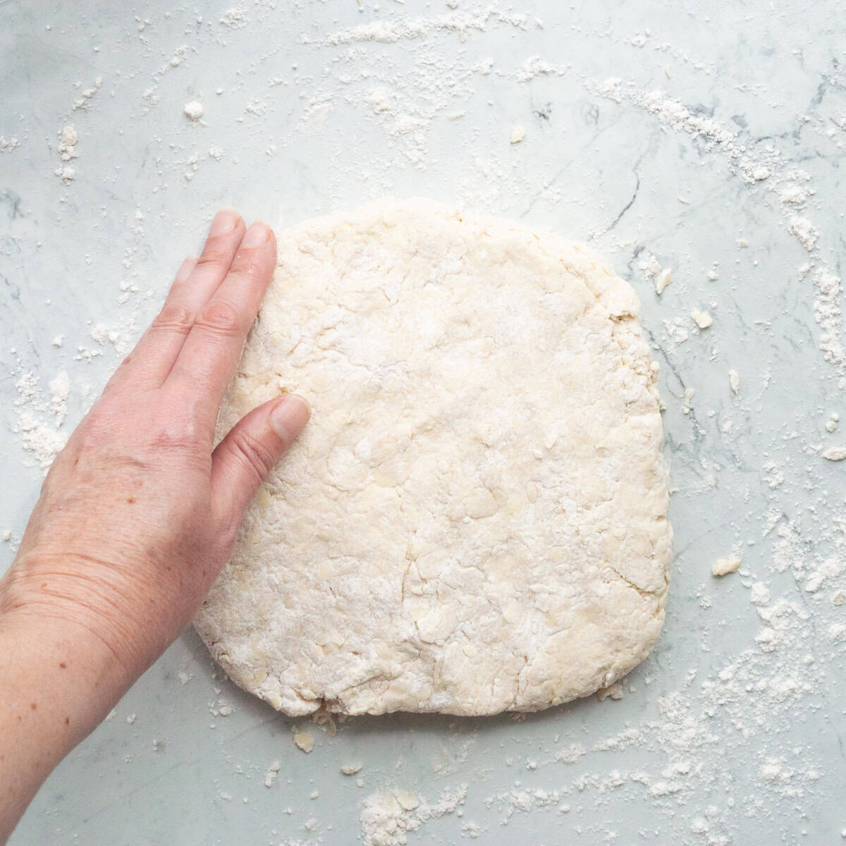 Patting biscuit dough into a square on a lightly floured surface.