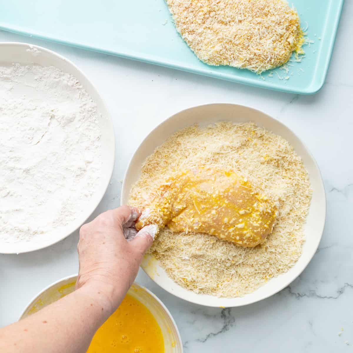 Dredging coated chicken into panko breadcrumbs.