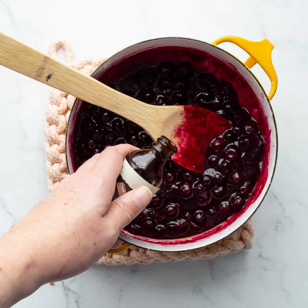 Adding vanilla extract to cooked blueberry compote in a yellow Dansk saucepan.