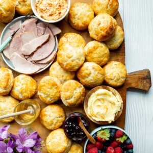 A brunch and breakfast biscuit board with biscuits surrounded by pimento cheese, ham, orange honey butter, blueberry compote, honey, and fresh berries.