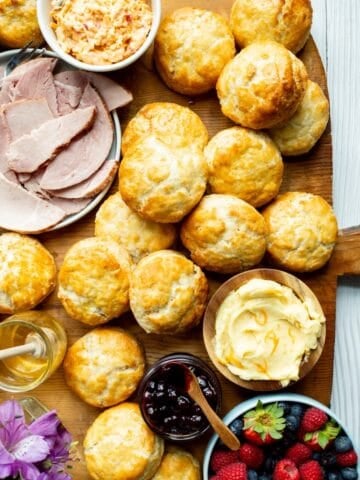 A brunch and breakfast biscuit board with biscuits surrounded by pimento cheese, ham, orange honey butter, blueberry compote, honey, and fresh berries.