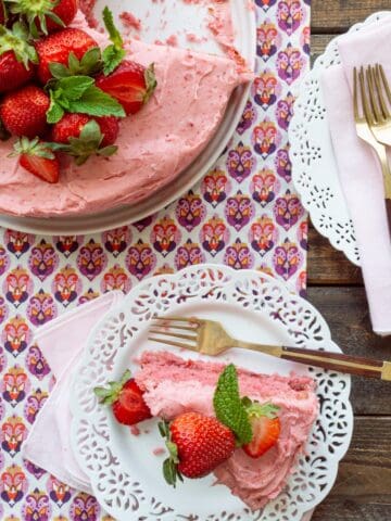 Strawberry cake with strawberry filling and strawberry buttercream on a white platter with a slice on white scalloped plate.