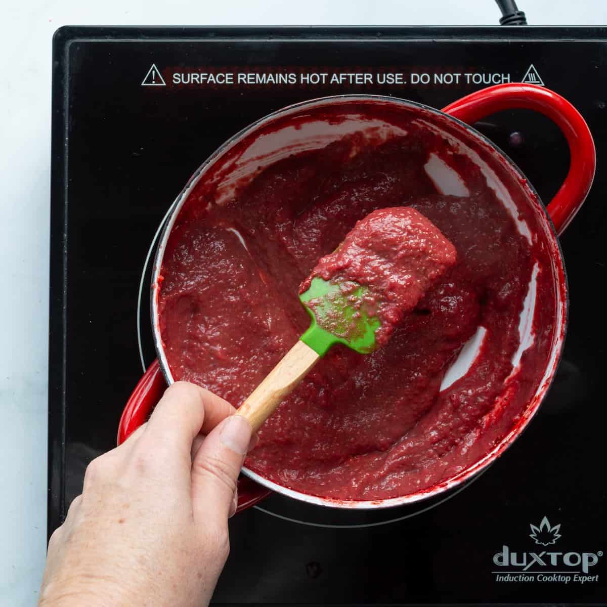 Reducing fresh strawberry puree to a tomato paste-like consistency in a red handled saucepan.