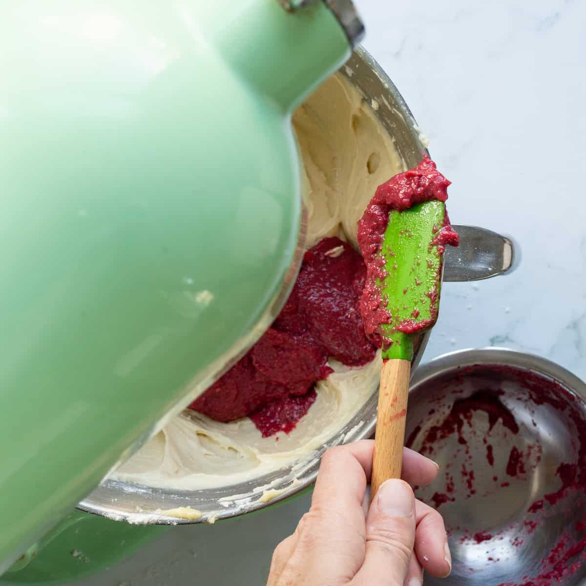 Adding strawberry reduction to cake batter in a mixer.
