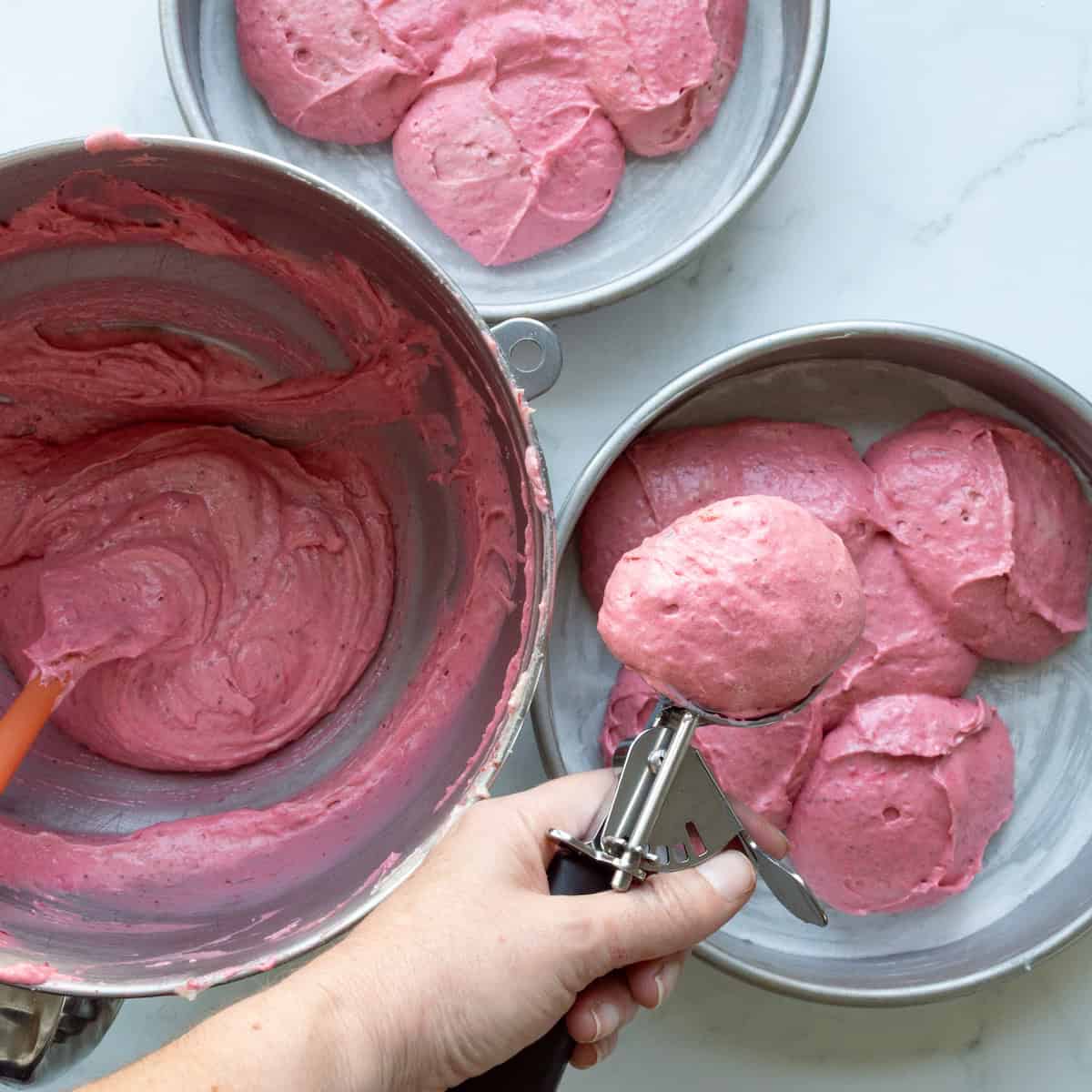 Dividing pink strawberry cake batter into two round bake pans.