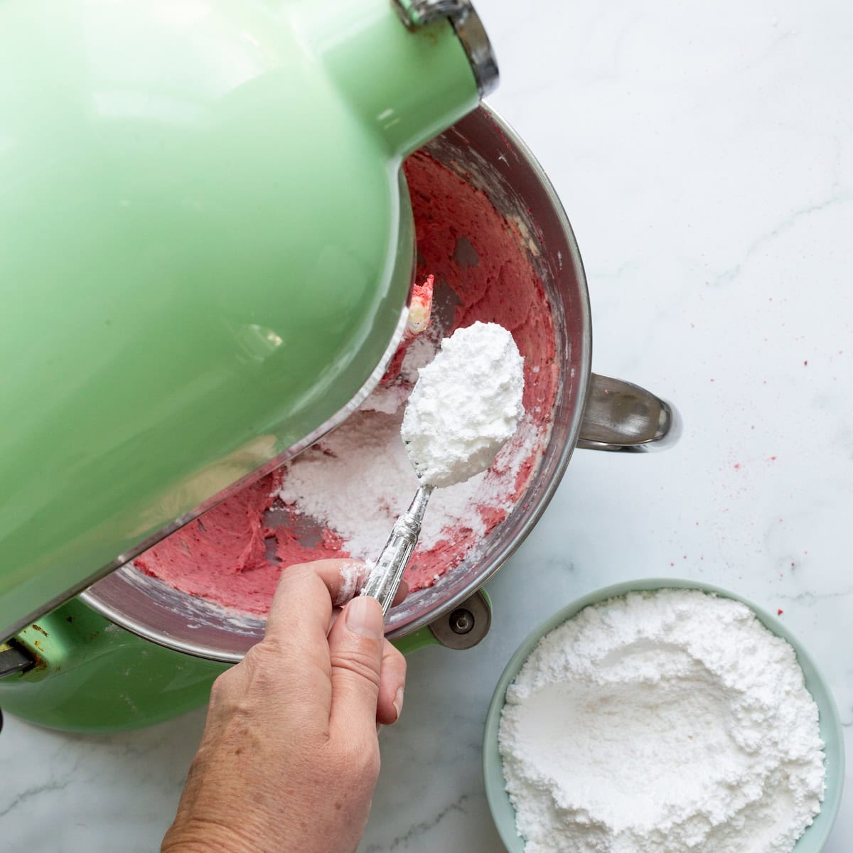 Adding powdered sugar to pink strawberry buttercream in a green mixer.