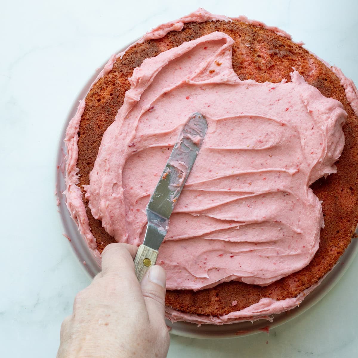 Spreading strawberry buttercream onto a strawberry cake.