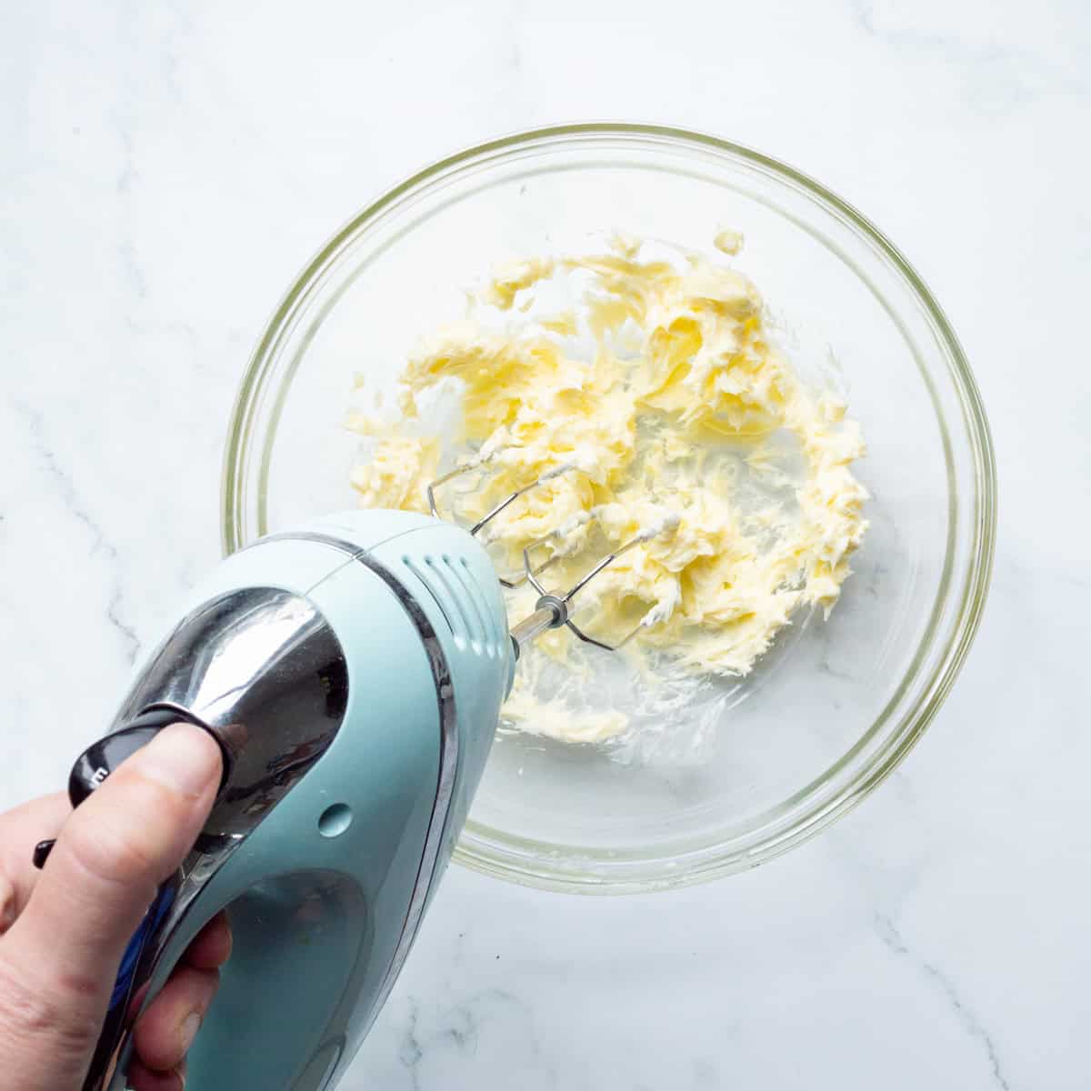 Creaming softened butter in a glass bowl with an aqua hand mixer.