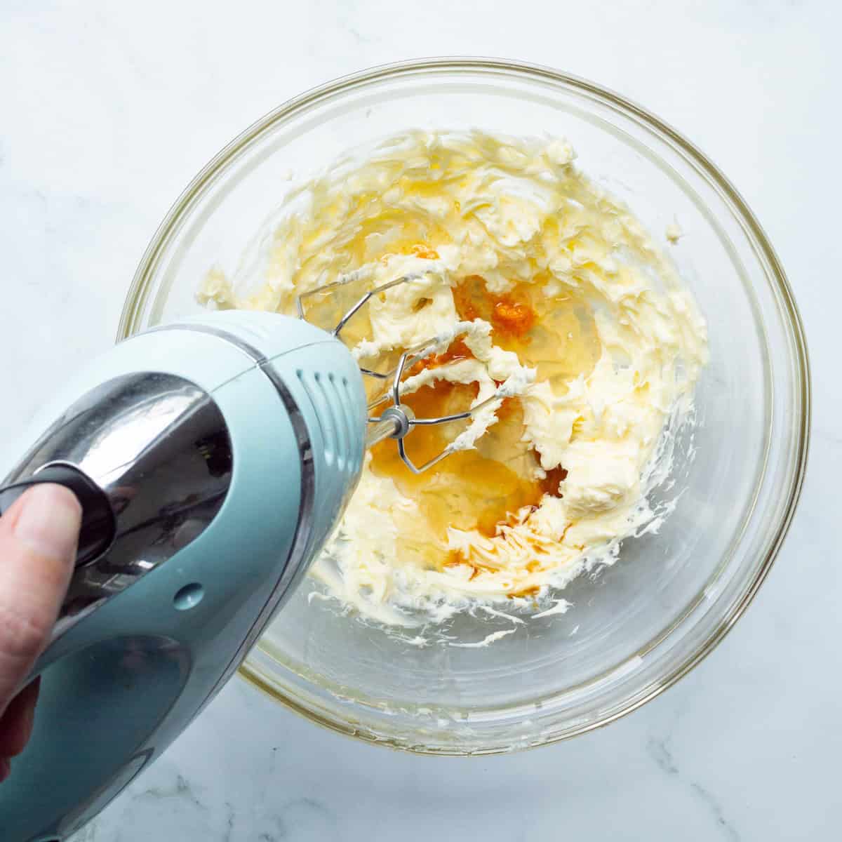 Beating honey, vanilla extract, and orange zest into softened butter in a glass bowl.