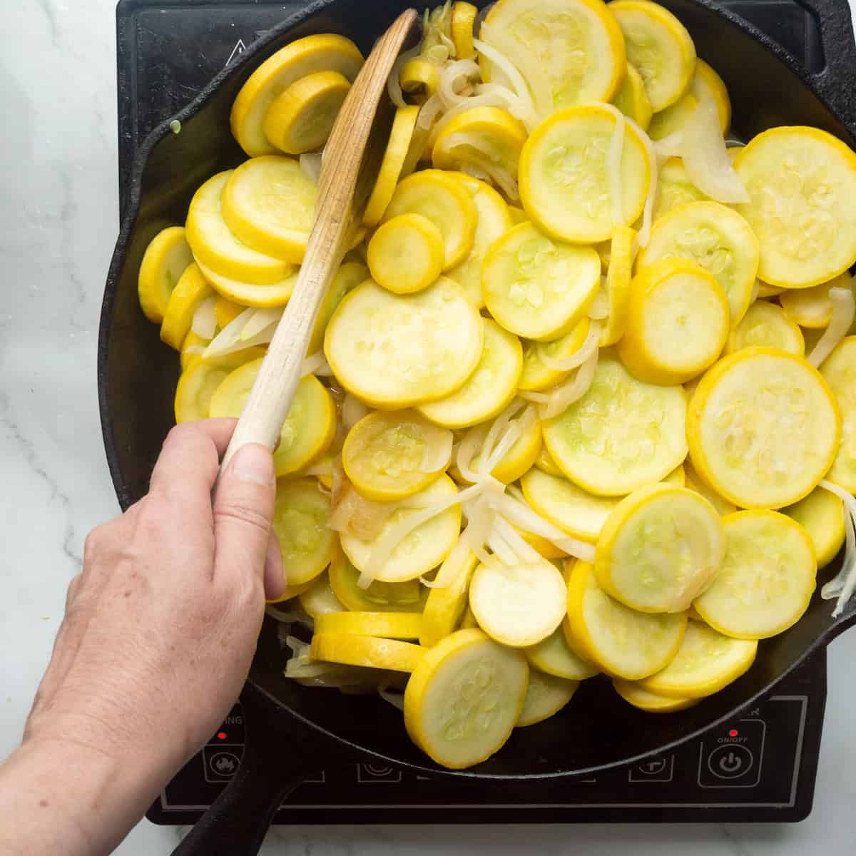 Cooking yellow squash and onions in a cast-iron skillet.