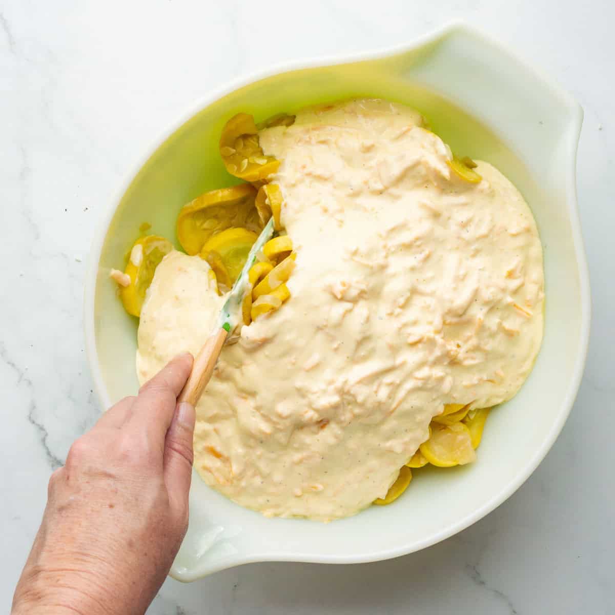 Combining cooked squash with creamy filling in a large bowl.