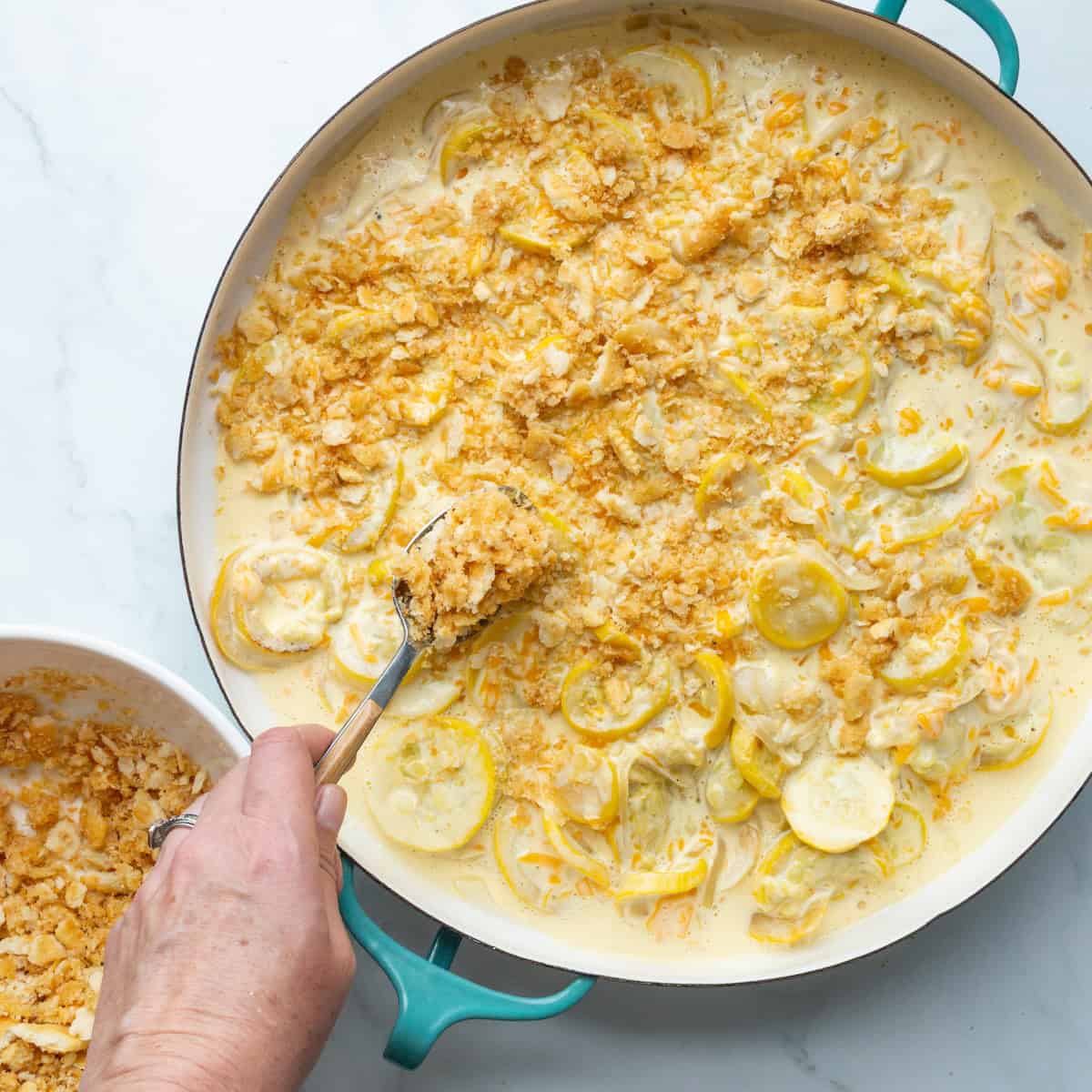 Sprinkling Ritz crackers onto squash casserole filling.