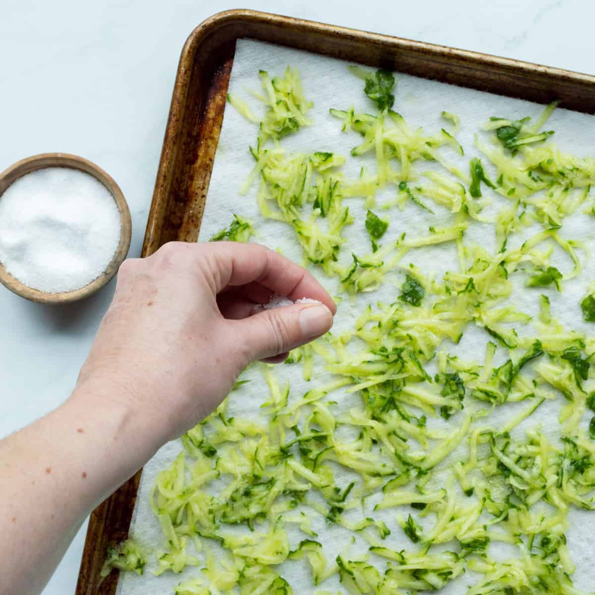 Sprinkling salt onto grated cucumber on a paper towel lined baking sheet.