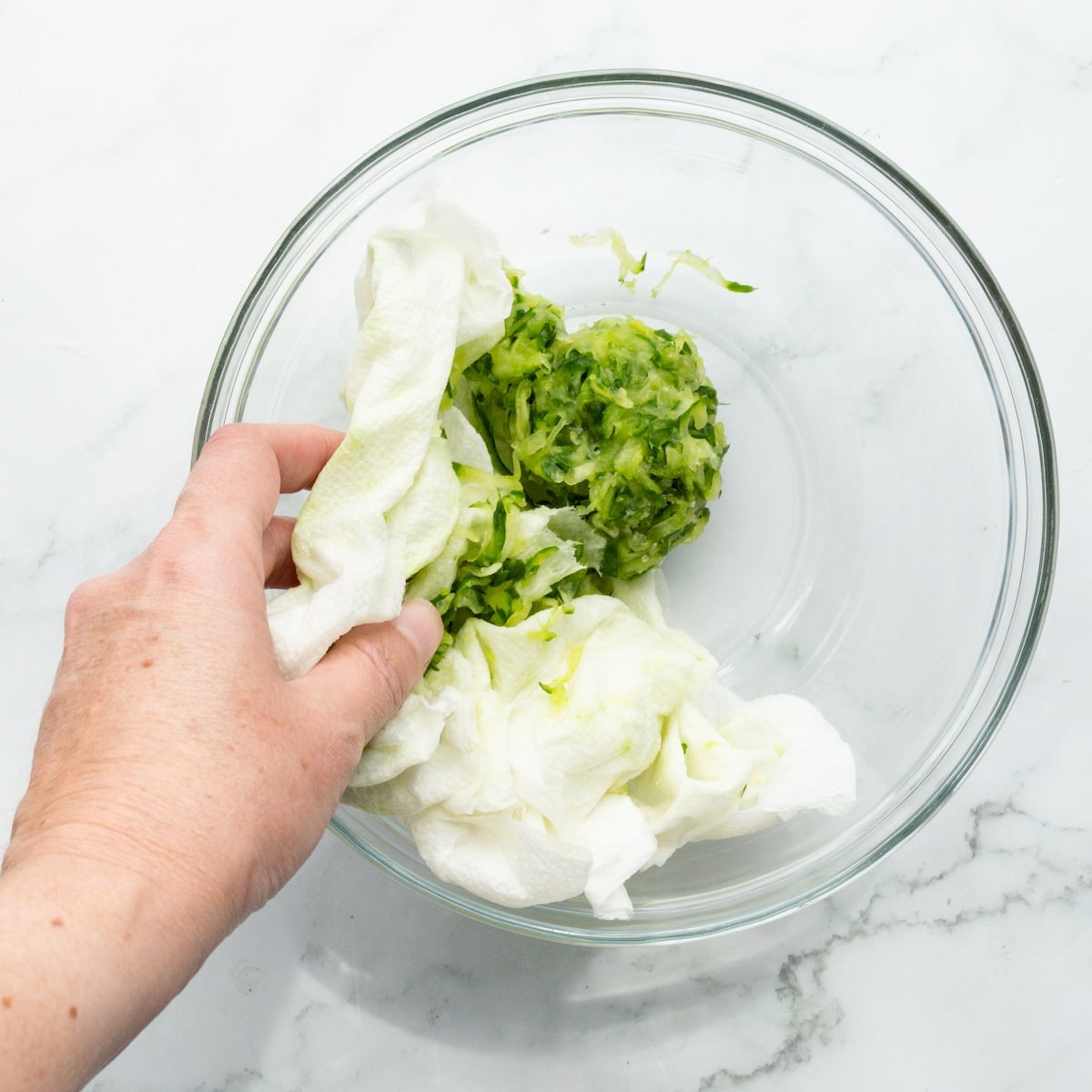 Unwrapping squeezed shredded cucumber in a glass bowl.