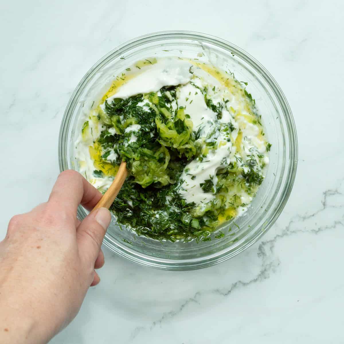 Stirring together all the ingredients for easy tzatziki sauce in a glass bowl.