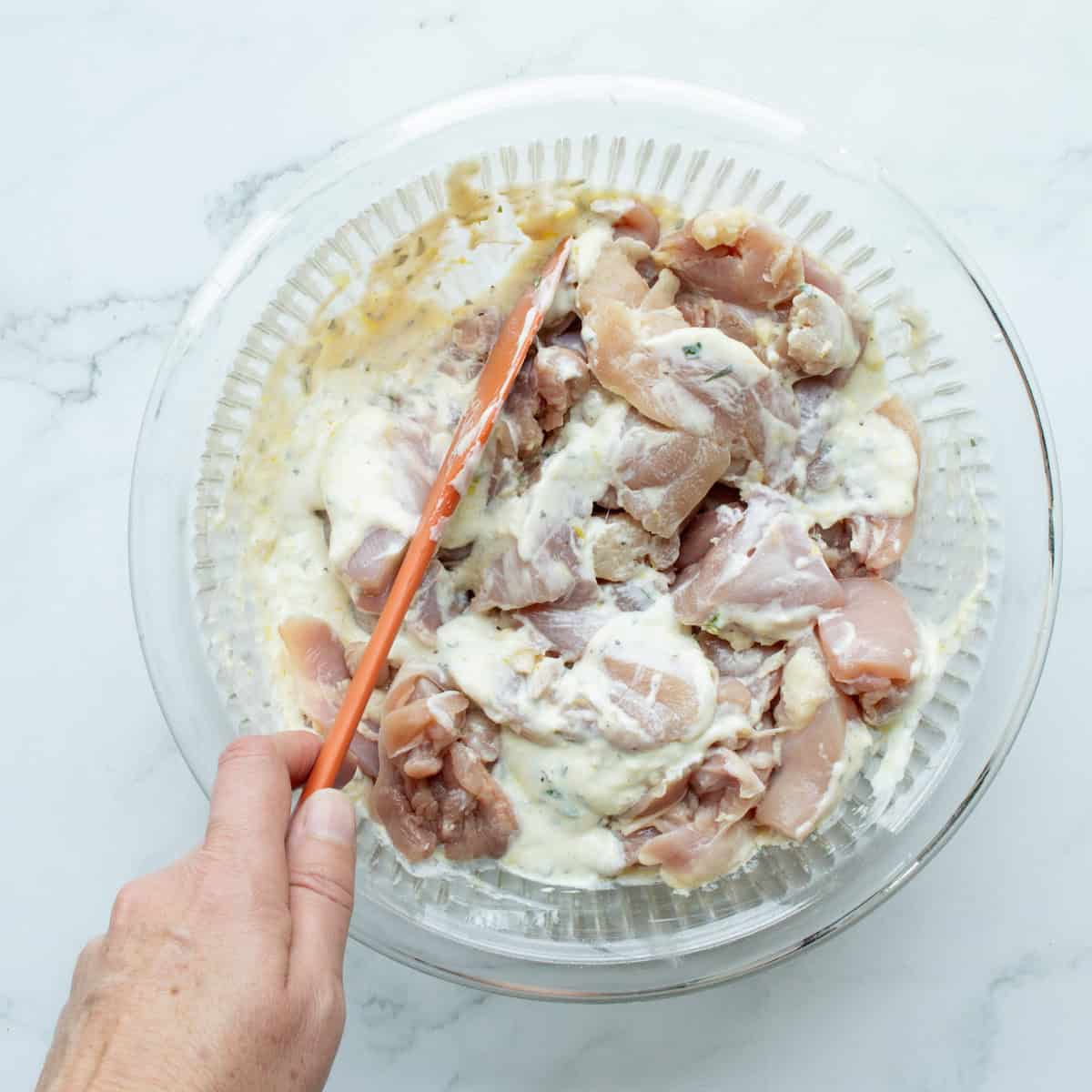 Combining pieces of chicken thigh with a yogurt marinade in a glass bowl.
