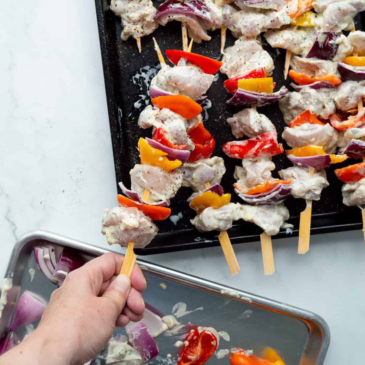 Adding skewers of chicken, peppers, and onion to a metal tray ready to be grilled.