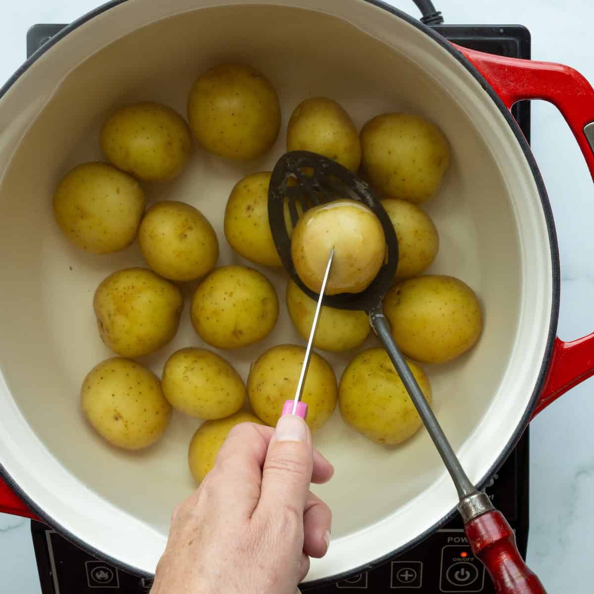 Checking the doneness of boiled potatoes in a large Dutch oven filled with water with a paring knife.