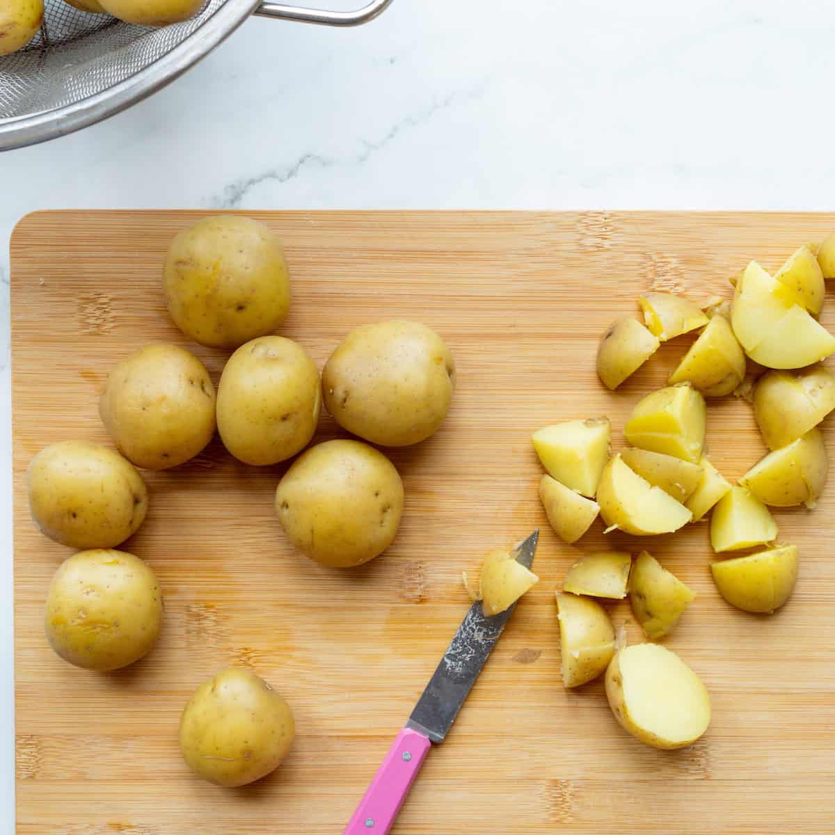 Cutting cooked Yukon Gold potatoes into small pieces with a pink handled paring knife.