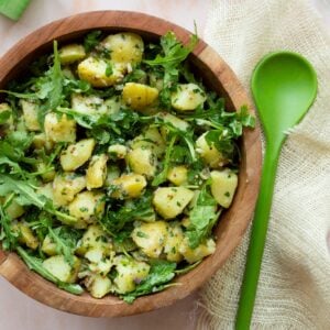 Mustard vinaigrette potato salad with arugula in a wooden bowl with a green serving spoon on the side.
