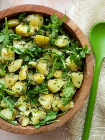 Mustard vinaigrette potato salad with arugula in a wooden bowl with a green serving spoon on the side.