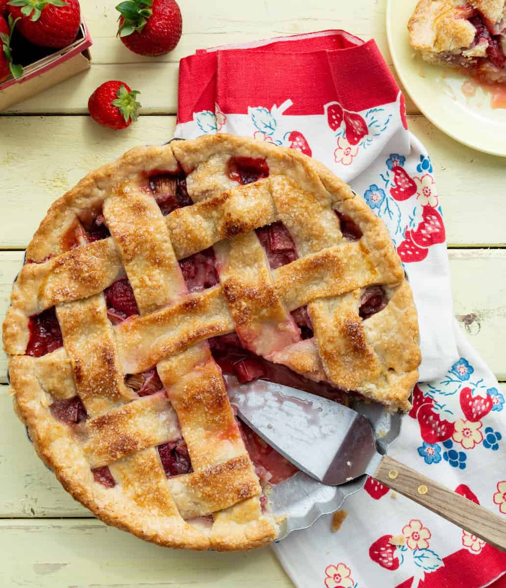 Lattice topped strawberry rhubarb pie with a slice out.